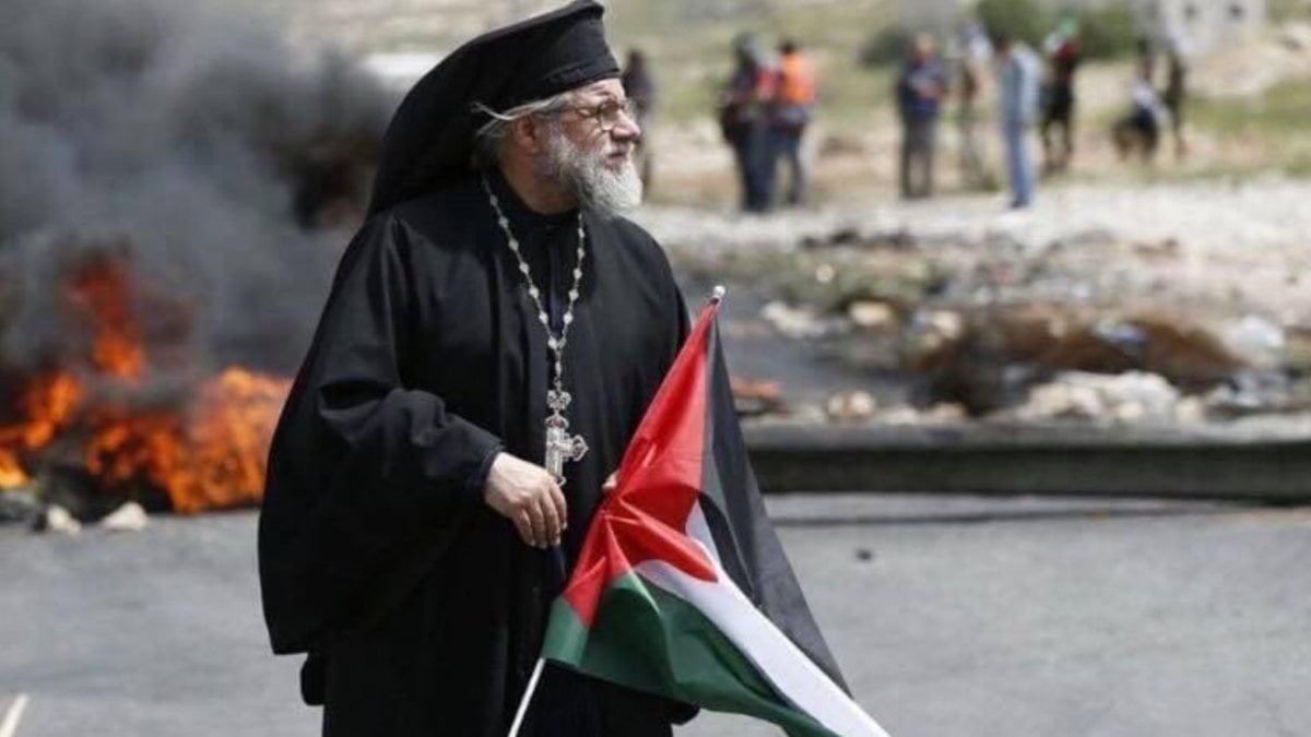 Catholic Archbishop Yulio stands before Israeli soldiers with the Palestinian flag